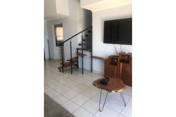 A staircase with a wooden finish and metal railings, a flat-screen TV mounted on the wall, and a small wooden table with a camera on it.