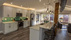 Una cocina moderna con armarios blancos, una isla central y un comedor con taburetes de bar.
