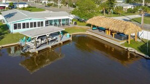 Propiedad frente al agua con una casa, un muelle y una construcción con techo de paja.