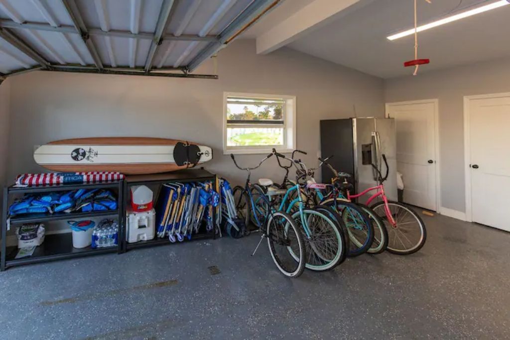 A garage with bicycles, a surfboard, and storage shelves.