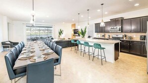 Una cucina moderna con mobili scuri, un'isola centrale e un'area pranzo con un tavolo lungo e sedie.