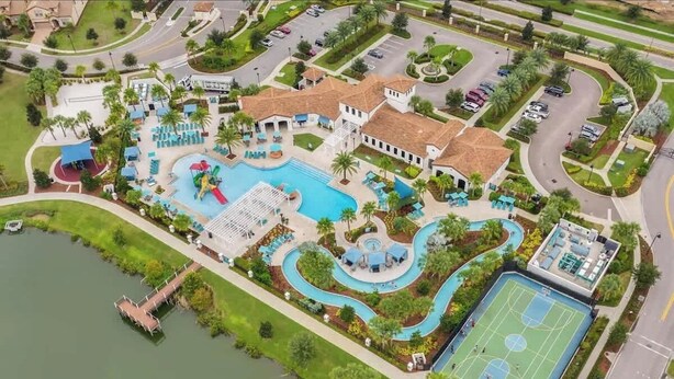 Vista aerea di un resort con piscina centrale, campo da tennis e molo che si estende su un lago.