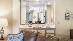 A living room with a brown leather couch, a coffee table, a large mirror, and a lamp. - Nonnie's Nest -     Peaceful Walk-In Condo Near Lake Taneyco (Branson)