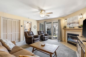 A living room with a fireplace, leather recliners, a ceiling fan, and a large window.