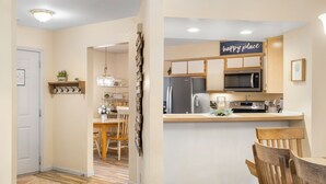 A kitchen with wooden cabinets, a stainless steel refrigerator, a microwave, and a sink. There is a sign above the sink that says "this is our happy place." - Nonnie's Nest -     Peaceful Walk-In Condo Near Lake Taneyco (Branson)