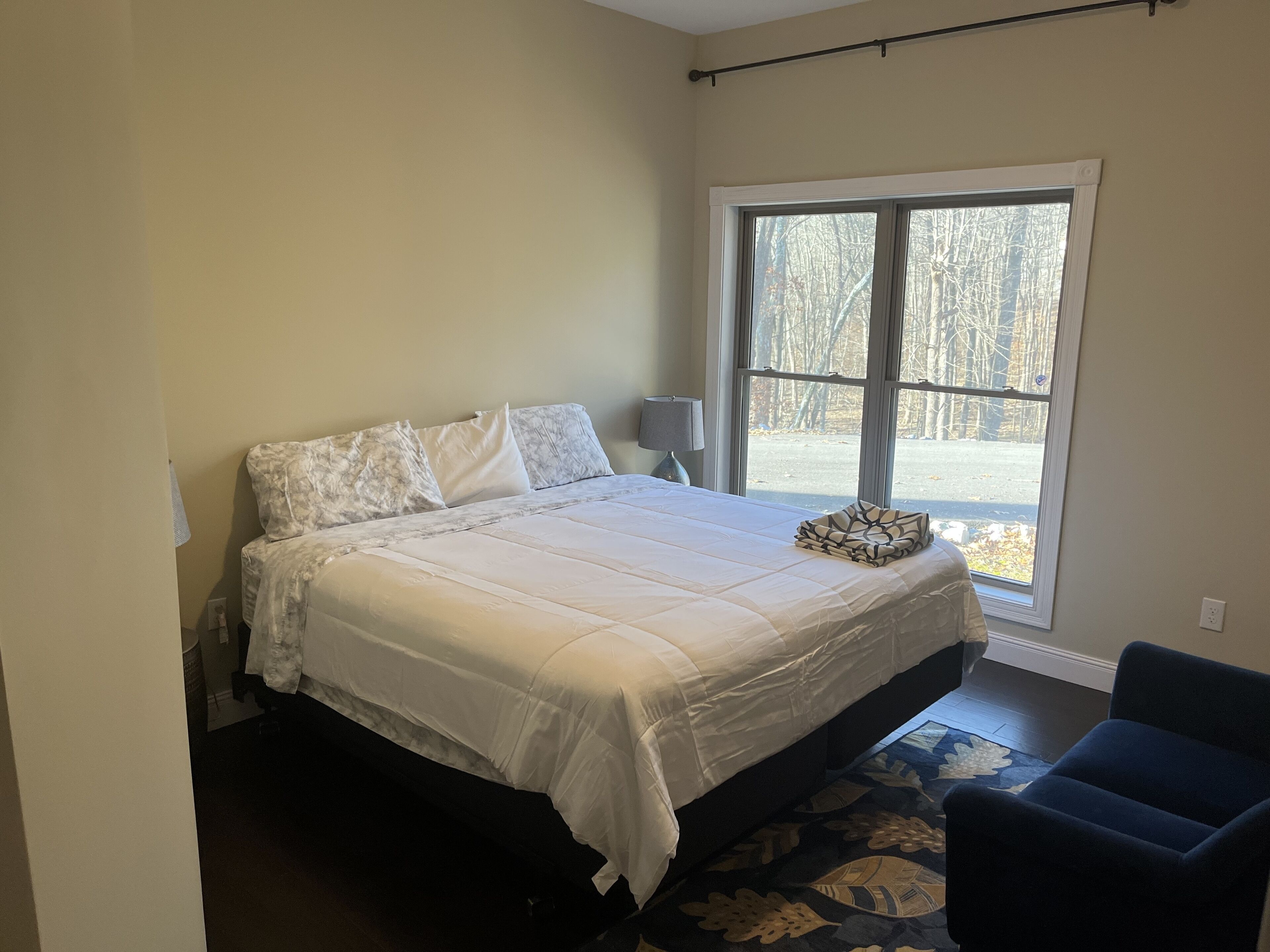 A bedroom with a bed, a chair, a window, and a lamp.