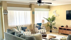 Ein Wohnzimmer mit Sofa, Sesseln, einem Couchtisch, einem Fernseher, einem Deckenventilator und einem Topfpflanzen.