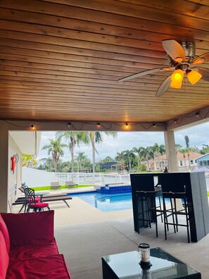A covered outdoor area with a pool, seating, and a ceiling fan.