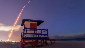 Ein Rettungsschwimmturm an einem Strand bei Einbruch der Dämmerung, mit sichtbarer Raketenstartbahn am Himmel.