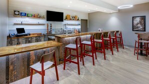 Een moderne bar met een houten toonbank, rode stoelen en een flatscreen aan de muur.
