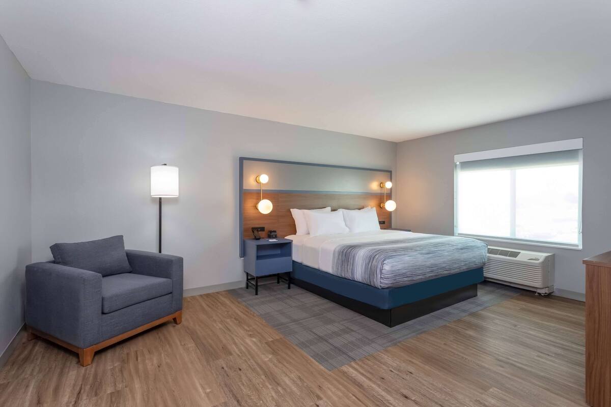 Ein modernes Hotelzimmer mit einem Bett, einer Couch, einem Nachttisch und einer Stehlampe.