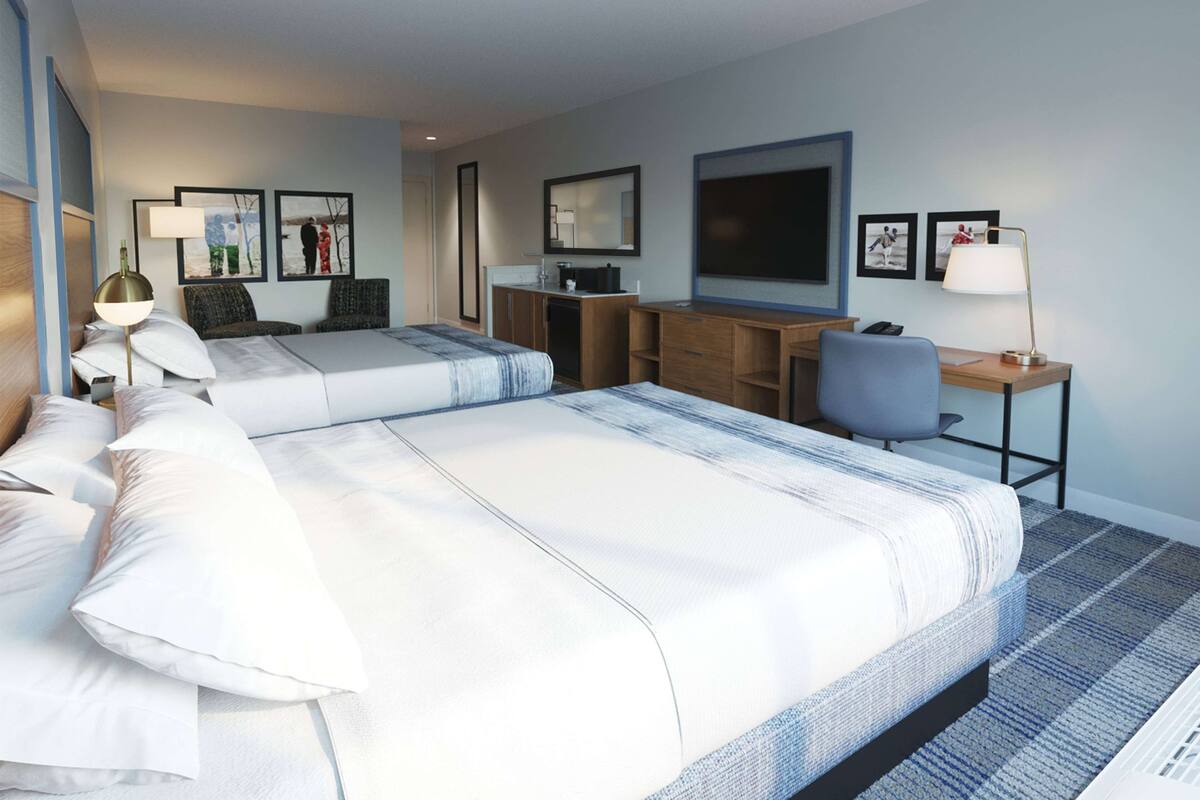 Ein Hotelzimmer mit zwei Betten, einem Schreibtisch, einem Stuhl, einem Fernseher und Kunstwerken an den Wänden.