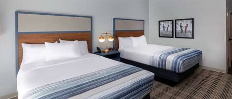 A hotel room with two beds, a nightstand with a lamp, and framed pictures on the wall.