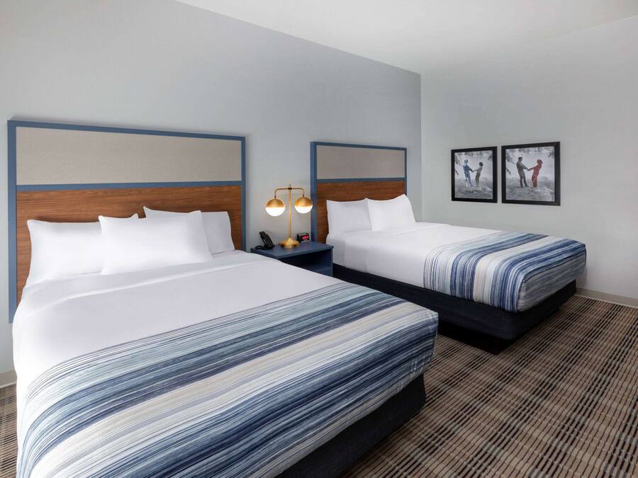 Habitación de hotel con dos camas, una mesita de noche con lámpara y cuadros en la pared.
