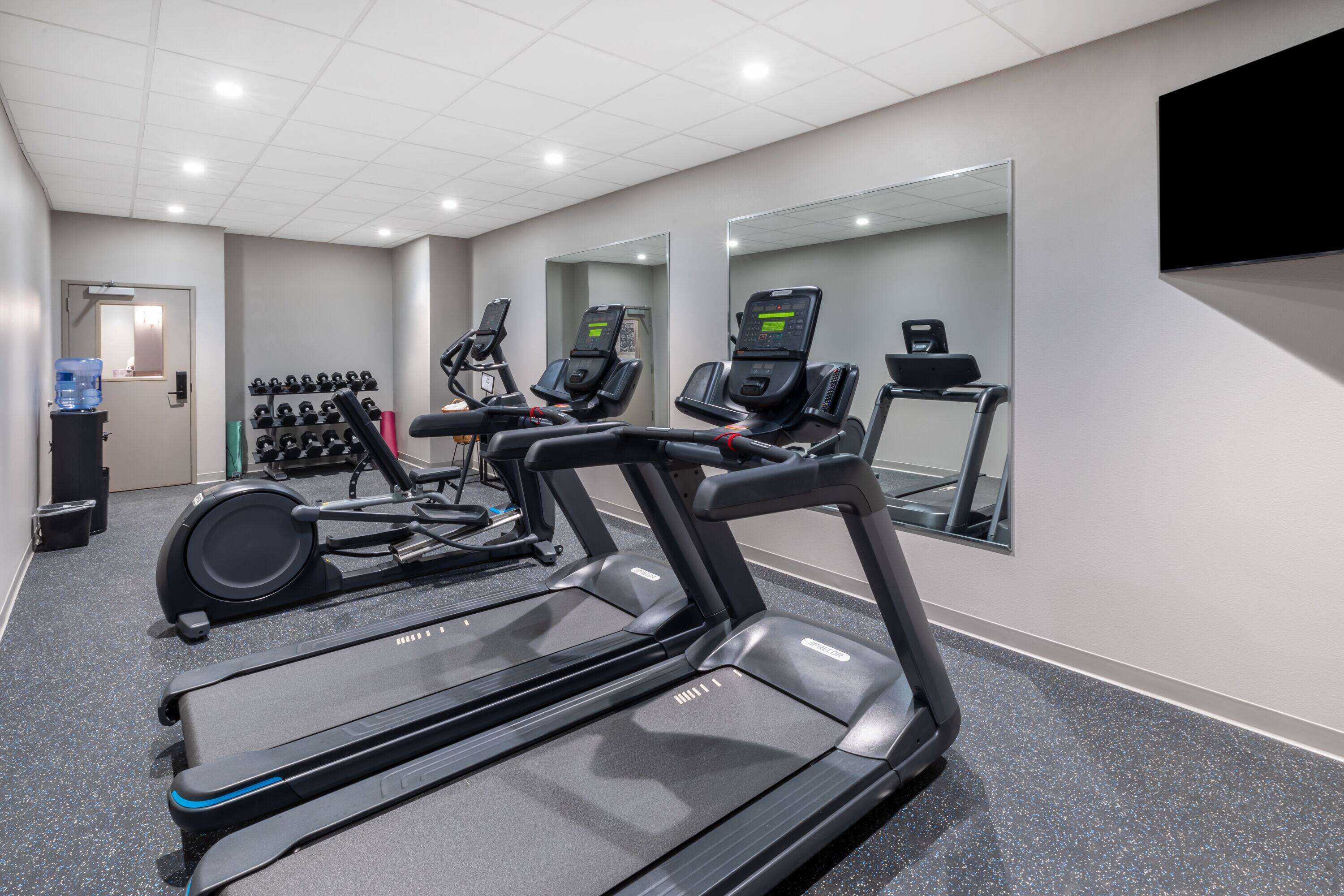 A gym with treadmills, elliptical machines, and a water dispenser.