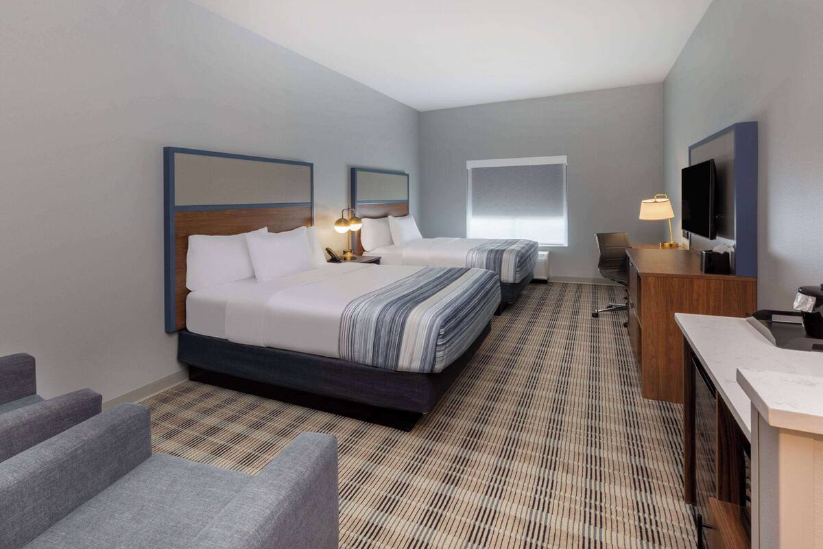 Ein Hotelzimmer mit zwei Betten, einem Schreibtisch, einem Fernseher und einer Sitzecke.