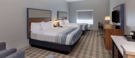 A hotel room with two beds, a desk, a TV, and a seating area.