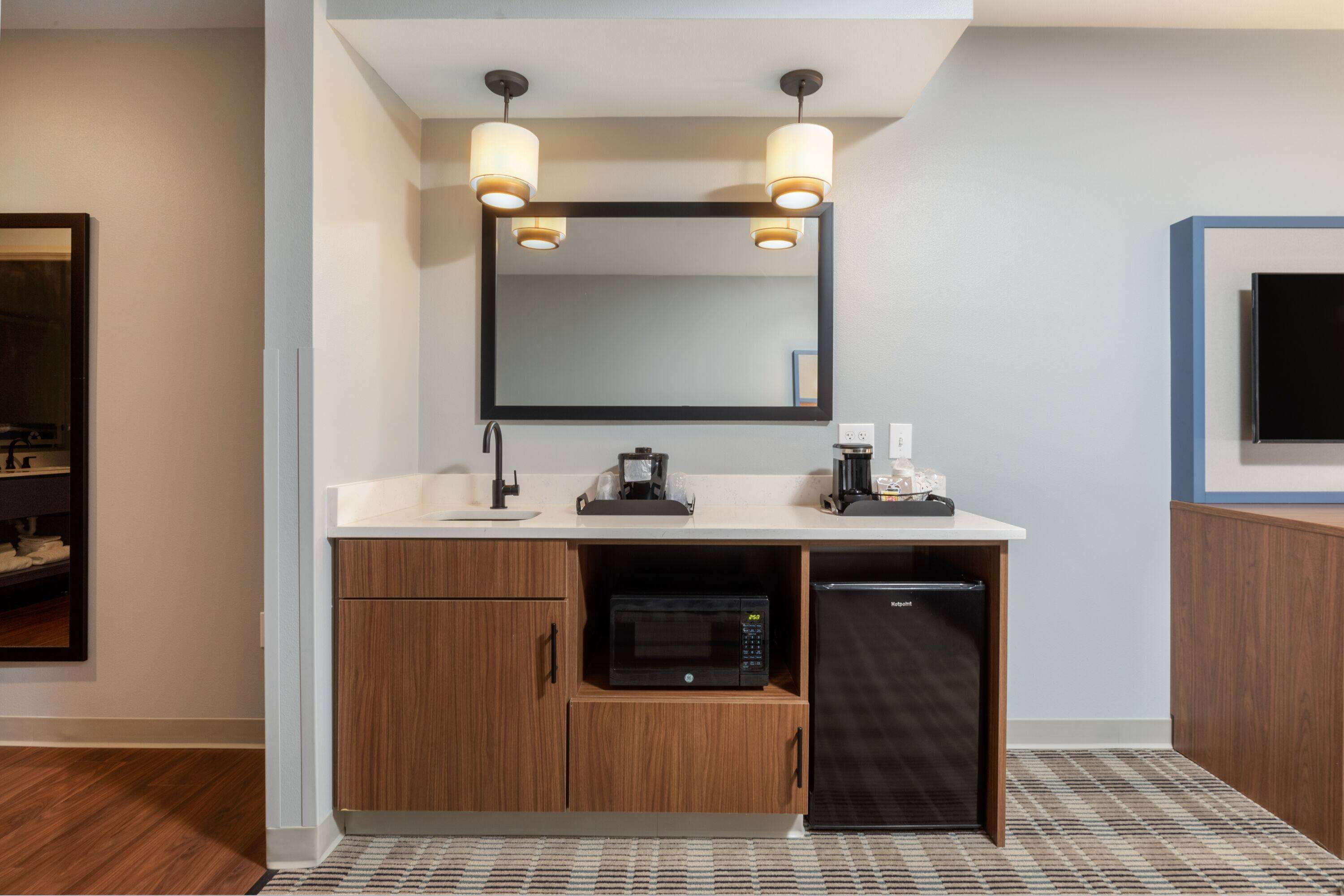 A modern bathroom with a double sink, a mirror, a microwave, and a refrigerator.