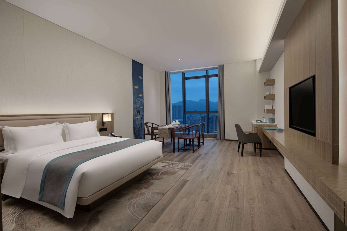 A modern hotel room with a large bed, a desk, and a TV.
