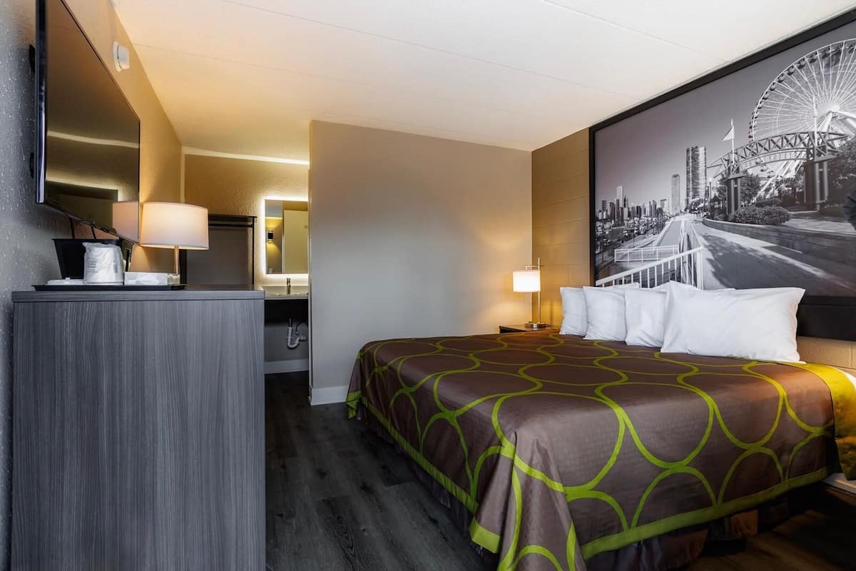 A hotel room with a bed, a desk, a mirror, and a cityscape painting on the wall.