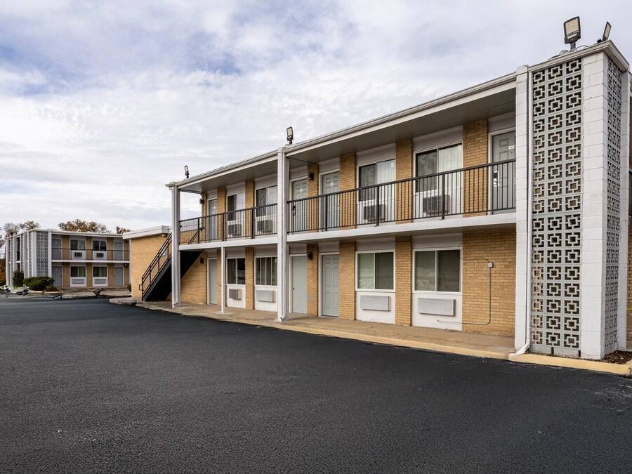 Ein Mehrstöckiges Motel mit einem zentralen Gang, Zimmern beiderseits und einem Parkplatz davor.