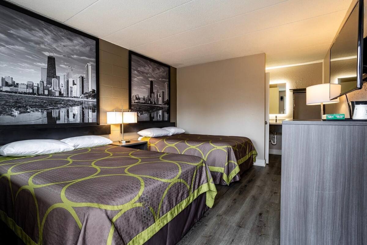A hotel room with two beds, a cityscape view, a desk, and a mirror.
