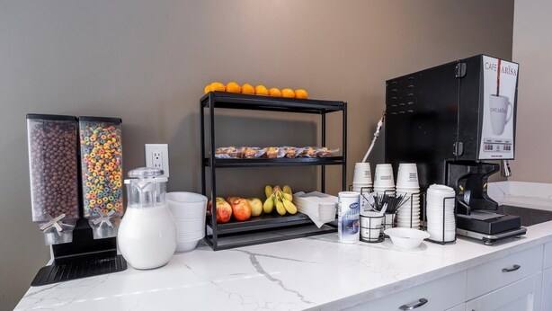 A breakfast bar with cereal, milk, fruits, and a coffee machine.