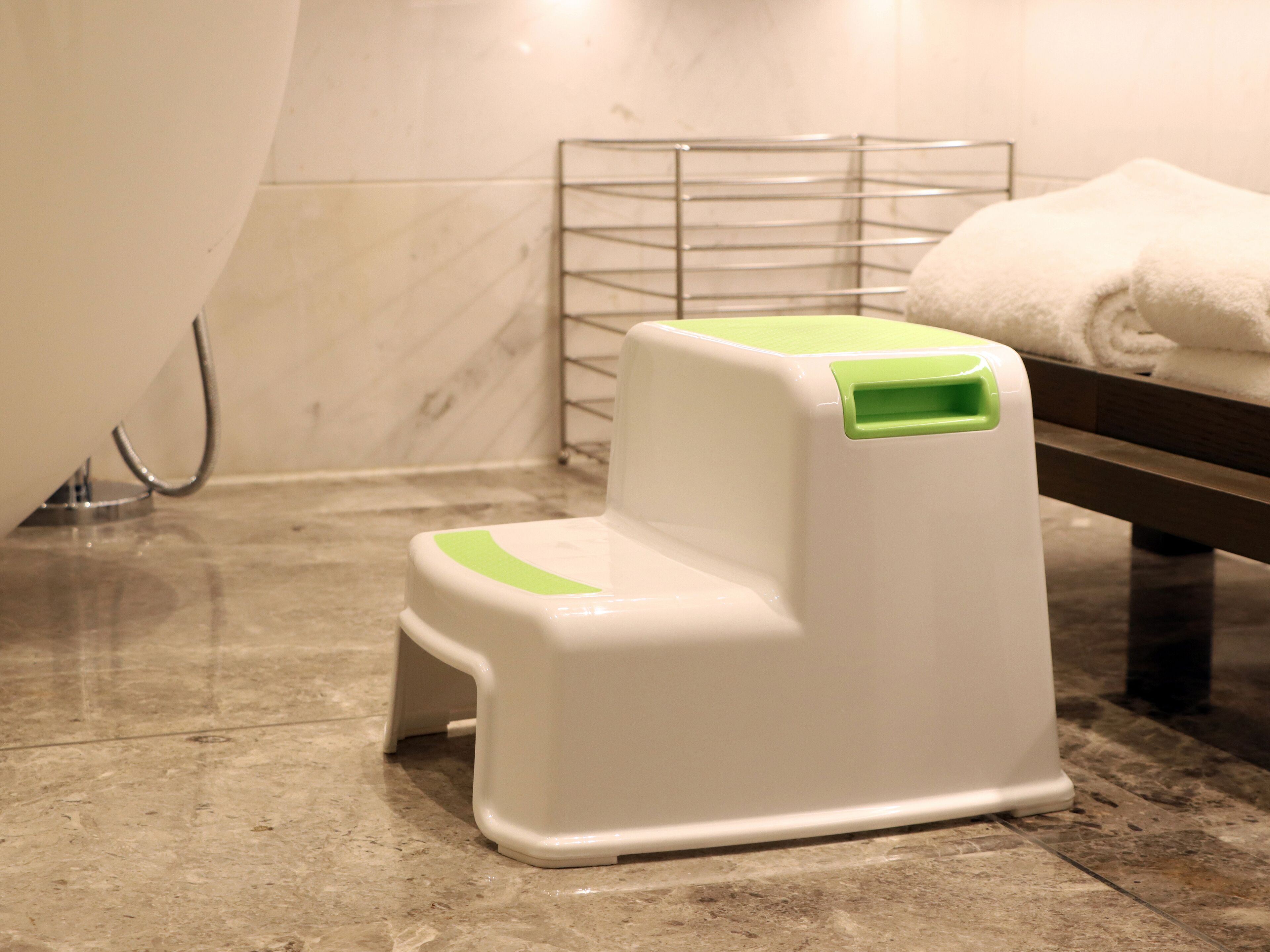 A white and green step stool in a bathroom with a marble floor, a metal rack, and a towel on the right.