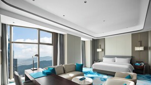 A modern hotel room with a large bed, a desk, a sofa, and a view of the mountains. - Wyndham Grand Zaozhuang (Zaozhuang)