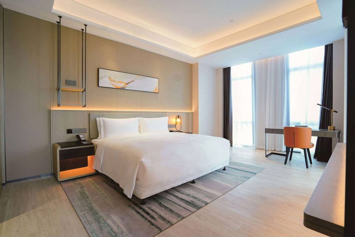 A modern hotel room with a large bed, bedside tables, a desk, and a chair.