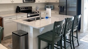 A modern kitchen with white cabinetry, stainless steel appliances, and a central island with bar stools.