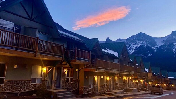 Une rangée de bâtiments en bois dotés de balcons, se dressant sur fond de montagnes enneigées et d’un ciel crépusculaire.