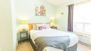 Une chambre à coucher comprenant un lit, deux lampes de chevet, une fenêtre avec des rideaux, un radiateur et un tableau accroché au mur.