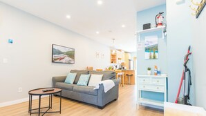 Un salon moderne avec un canapé gris, une petite table ronde et un coin cuisine à l’arrière-plan.