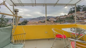 Ein Balkon mit gelber Wand, einem Hängesessel und einem Tisch mit Stühlen.