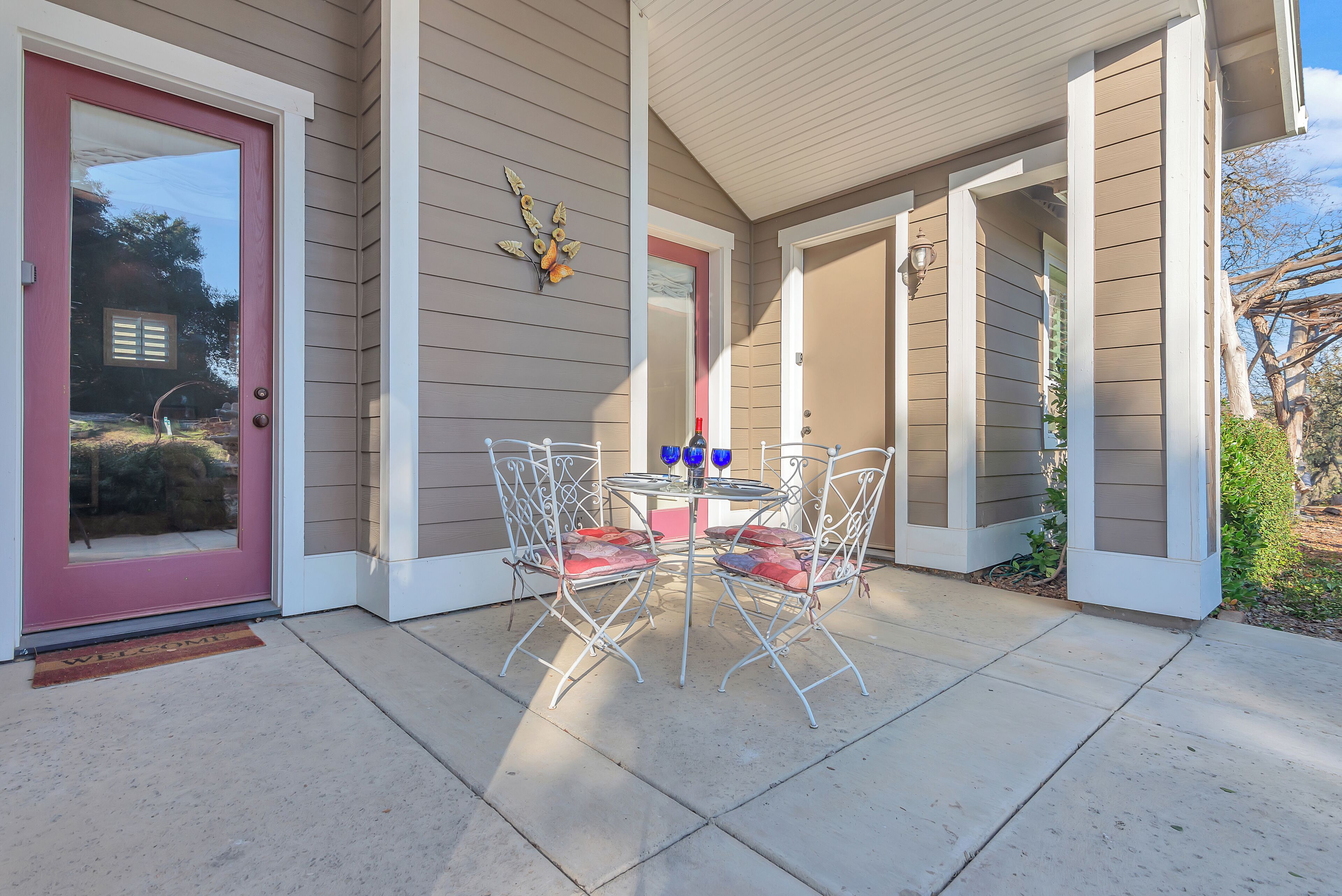 A covered patio with a table and chairs, a welcome mat, and a decorative wall piece.