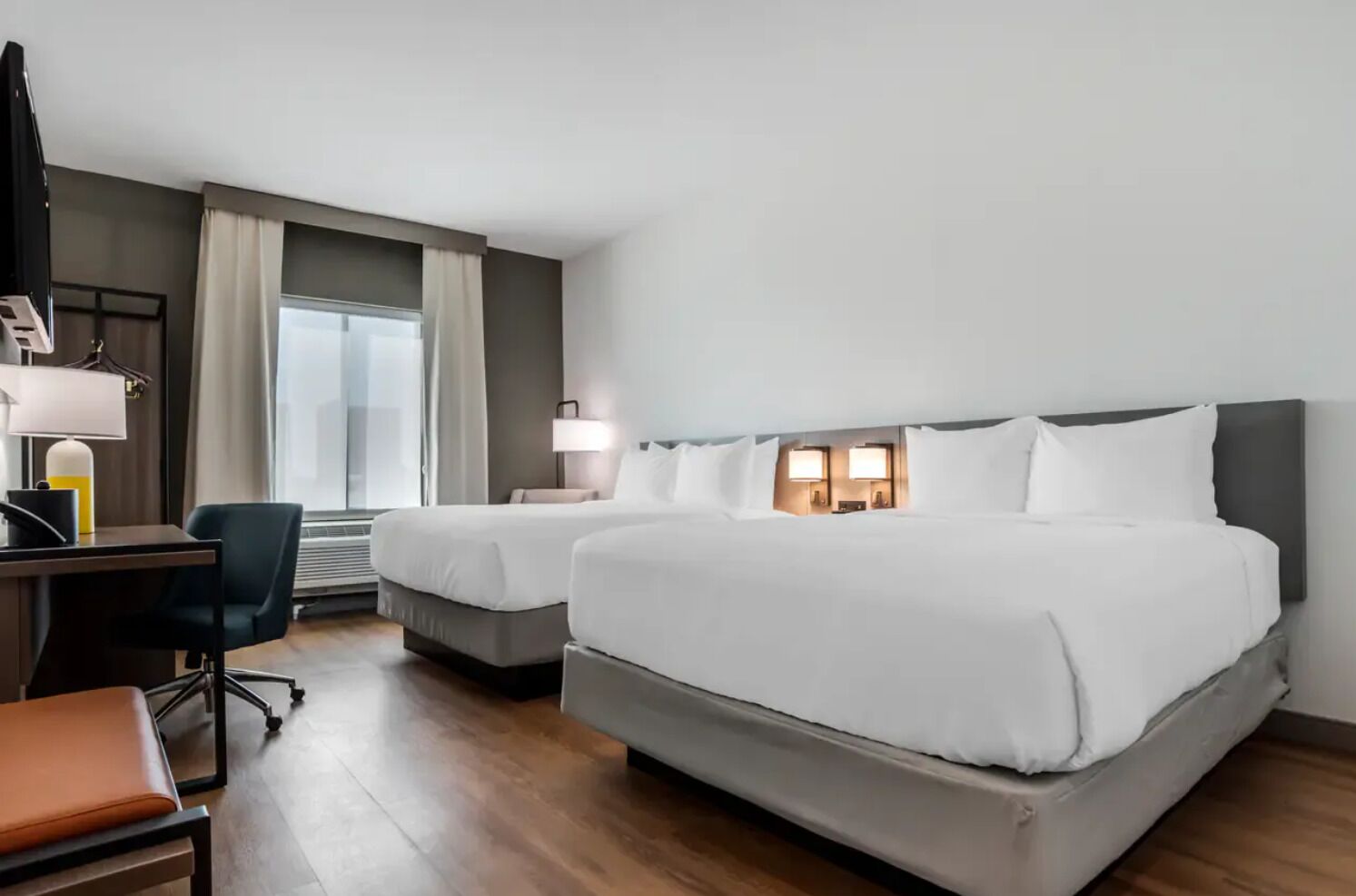 Une chambre d’hôtel avec deux lits, un bureau avec une chaise, une lampe et une fenêtre avec des rideaux.