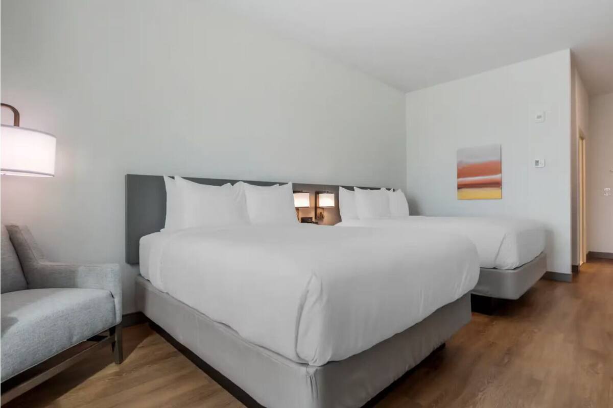 A hotel room with a large bed, a smaller bed, a sofa, and a painting on the wall.