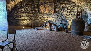 A stone-walled room with a rustic interior, featuring a wooden chair, a large barrel, and various wooden objects. - Les Vignes de Théonie (VILLIE-MORGON)