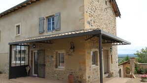 A stone house with a covered patio, a door, and a window with shutters. - Les Vignes de Théonie (VILLIE-MORGON)