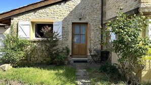 Een stenen gebouw met een houten deur en luiken, een kleine tuin en een bord waarop staat 'Gîte de France'.