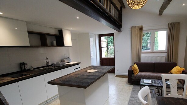 Een moderne keuken met een centraal eiland, witte kasten, en een zithoek met een bank en stoelen.