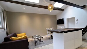 Een moderne woonkamer met een bank, een kleintje tafel, en een keukenhoek met een aanrecht en stoelen.