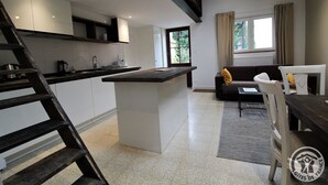 Een moderne keuken met een centraal eiland, een zithoek met een bank en tafel, en uitzicht op de omgeving door een raam.