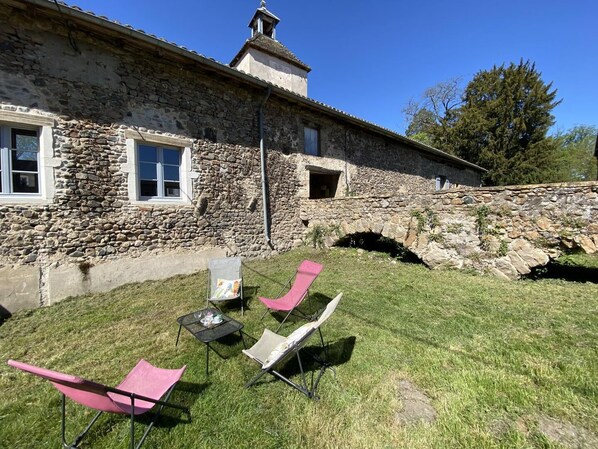 Un edificio in pietra con un piccolo arco, un prato e due sedie rosa.