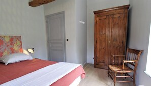 Une chambre à coucher comprenant un lit, une armoire en bois, une chaise et une lampe fixée au mur.