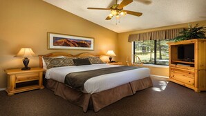 Une chambre à coucher comprenant un lit, deux tables de chevet, un ventilateur de plafond, une fenêtre avec vue et une armoire en bois.