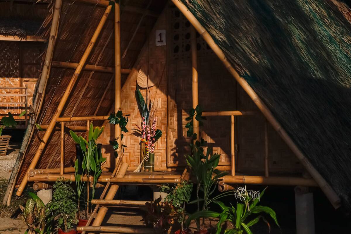 Eine traditionelle Bambushütte mit einem Reetdach, umgeben von tropischen Pflanzen.
