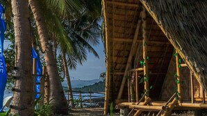 Une cabane rustique à toit de chaume, entourée de palmiers et offrant une vue sur la plage.