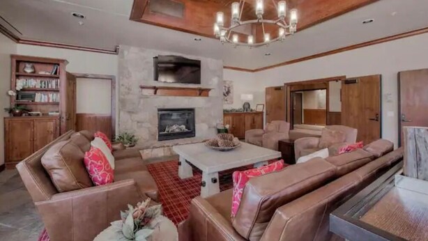 A spacious living room with leather sofas, a stone fireplace, and a chandelier.